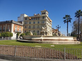 Statue by fountain against building against clear blue sky