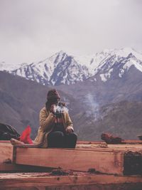 Woman sitting on snowcapped mountain against sky