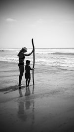 Side view of mother with son holding stick at beach against sky