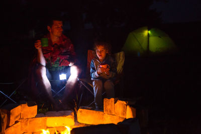 People sitting by bonfire at night