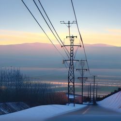 Power lines following road with mountains in the background duing sunset