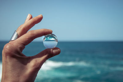 Cropped image of hand holding crystal ball against sea