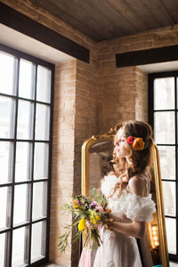 Woman holding flower bouquet against wall