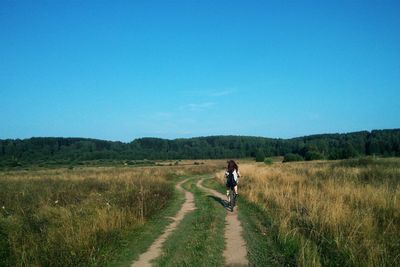 Man riding bicycle on road amidst field against clear sky