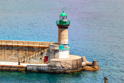 Lighthouse by sea against blue sky