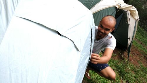 Smiling young man arranging tent on field during camping