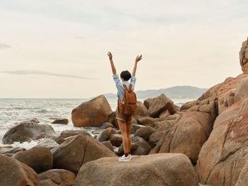 Rear view of woman standing on rock at beach