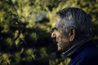 Side view of senior man looking away against trees in forest