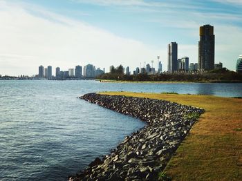 View of city at waterfront against cloudy sky