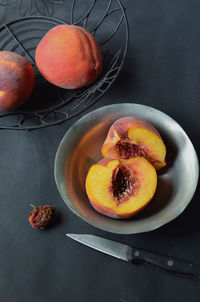 Peaches in black wire basket and halved peach in pewter bowl, knife and peach pit