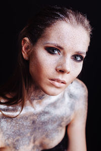 Shirtless young woman with silver glitter on her body against black background