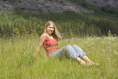 Portrait of happy woman sitting on grassy field against mountain