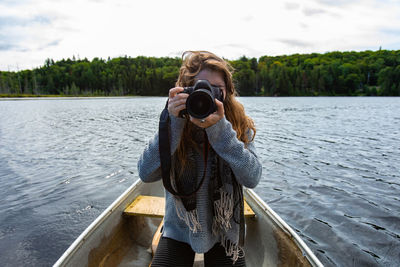 Woman photographing by lake against sky