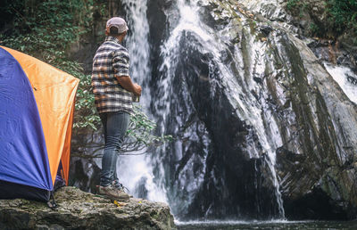 Male tourist standing and drinking coffee at the waterfall