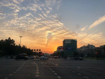 Cars on street against sky at sunset