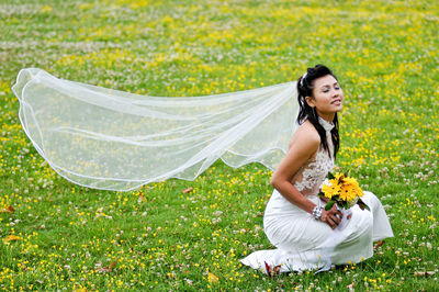 Bride with closed eyes holding bouquet while crouching on grassy field