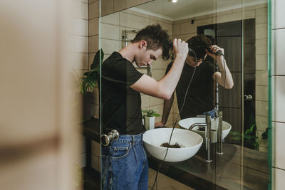 Man with electric razor cutting his own hair in bathroom