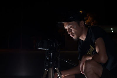 Man sitting in illuminated lighting equipment against black background