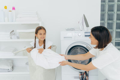 Mother with daughter washing clothes in machine at home