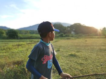 Side view of boy standing on field against sky