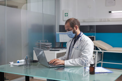 Doctor wearing mask using laptop in clinic