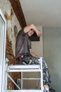 Smiling male worker sitting on ladder in break at site