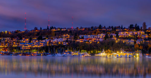 Illuminated city by river against sky