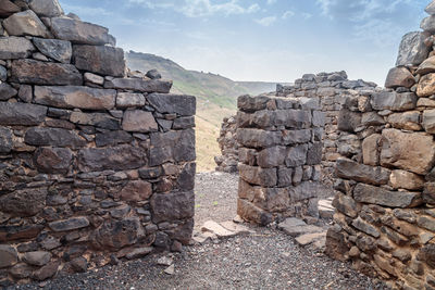 Stone wall by rocks against sky