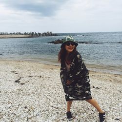 Portrait of smiling young woman standing at beach against sky