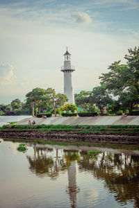 Lighthouse by lake and building against sky