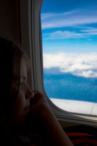 Thoughtful girl sitting by window in airplane