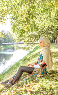 Side view of smiling young woman sitting by lake