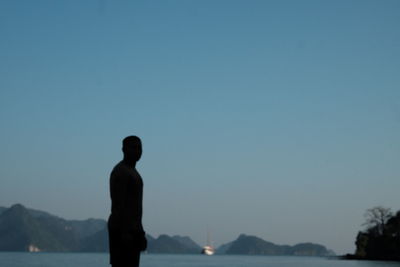 Silhouette man standing by sea against clear blue sky