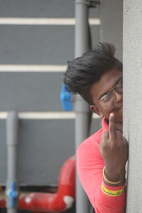 Portrait of man showing obscene gesture while standing behind wall