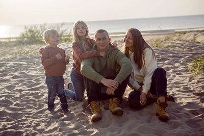 Family with a son and daughter and a dog sit on the sand in autumn
