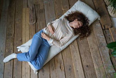 Beautiful young calm woman sleeping, napping during day on mattress on wooden floor at cozy home