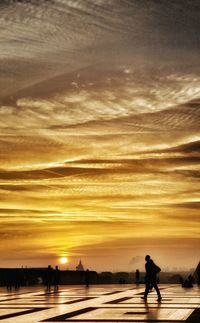 Silhouette people walking on shore against sky during sunset