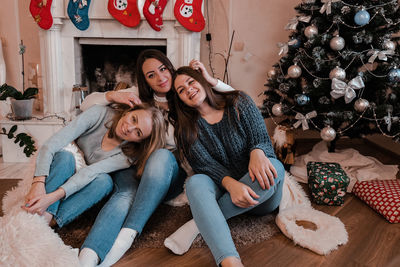 Tree young woman girls sitting next to the fireplace and christmas tree. having fun, togetherness