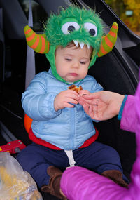 Tailgating baby monster is having some snacks in the back of the car on halloween