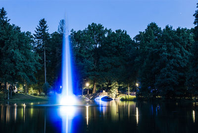 Illuminated trees by river against sky at night
