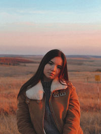 Portrait of young woman standing against sky during sunset