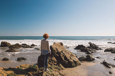 Rear view of woman standing at beach against clear sky