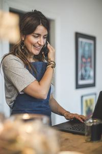 Smiling female owner taking order through mobile phone at counter in deli