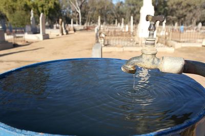 Water flowing from old faucet in container against cemetery