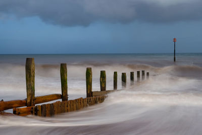 Wooden posts on beach against sky