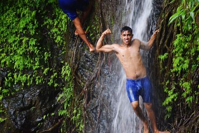 Full length of shirtless man splashing water in forest