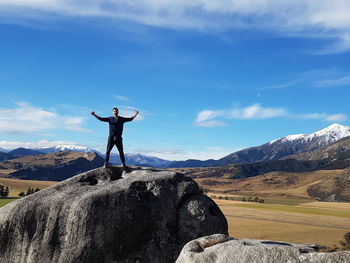 Man with arms outstretched standing on rock against cloudy sky