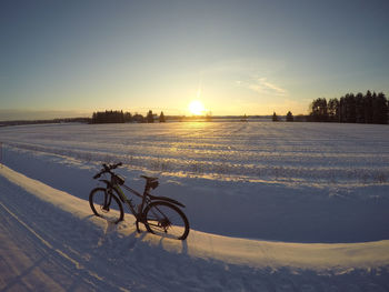 Bicycle on snow covered field against sky during sunset