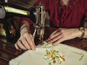 Senior lady in glasses using retro sewing machine to create linen napkin in cozy room at home