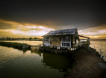 Building by lake against sky during sunset